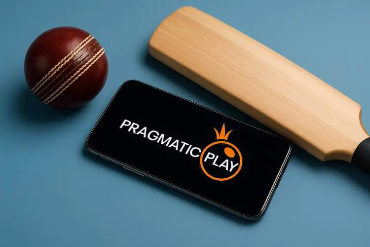 A photo of a smartphone displaying the Pragmatic Play logo lies beside a polished red cricket ball and a wooden cricket bat, captured under soft studio lighting.